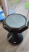 Photo of black wobble stool showing octagonal seat with geometric textured pattern on top and stable, flared base with gold label.