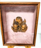 Wooden shadow box with three sculpted angel heads mounted on pink satin lining, showing full shadow box and angel cluster in center.