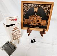 Photo of the Berlin Wall piece in protective museum bag beside original box and framed Semperoper Dresden brass metal artwork on easel.