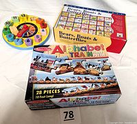 Three educational toys displayed: Melissa & Doug Alphabet Train puzzle box, wooden clock with shaped number slots, and Discovery Toy Bears, Boats & Butterflies alphabet puzzle boxed set.