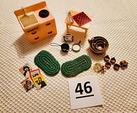 Photo of the pink and white dollhouse kitchen sink with black accents, small wooden table with checkerboard game, miniature kitchen accessories including nesting bowls, mugs, and kitchen utensils along with two green rugs and decorative floral pieces.