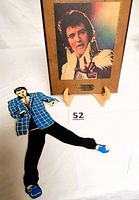 Photo of the wooden picture plaque of Elvis Presley with "The King 1935 1977" inscription, standing on a small wooden easel.