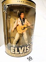 Front view of Elvis Presley Teen Idol doll in original packaging showing the doll, guitar, microphone graphic, and decorative musical notes on packaging.