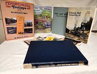 Photo displaying a group of six train books and three brochures relating to railroads, spread out on a white surface, showing titles and cover designs.