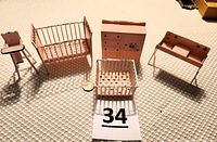 Photo of pink vintage nursery dollhouse furniture including crib, bureau, playpen, high chair, and bench all decorated with multi-colored dots and lamb illustrations.