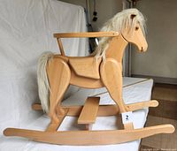 Side view of the oak wood rocking horse showing the safety guard-rail seat, faux fur mane and tail, and step-up platform on curved rockers.