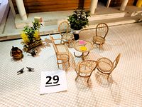 Miniature outdoor wicker furniture set including loveseat, 4 chairs, round table, planters, mailbox, copper teapot, watering can, plates, pigeons arranged on textured surface.