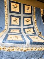 Full view of the quilt showing 8 carousel horse blocks with two alternating designs on a blue and white printed background with carousel print border.