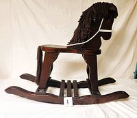 Side view of mahogany-colored wooden rocking horse showing brown yarn mane and tail, leather ears, rope rein, and smooth wood finish.