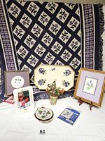 Full lot showing violet-themed Afghan backdrop with items arranged including framed art, ceramic planter, wooden tray, picture frames, cross stitch pieces, paperweight