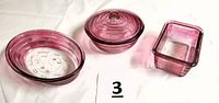 Three cranberry colored Glasbake baking dishes: small oval, round covered dish with knob, and rectangular dish.