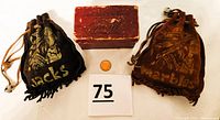 Photo showing the two suede leather pouches labeled 'Jacks' and 'Marbles' with stamped Indian Chief heads, a small vintage burgundy box, and a coin for scale.