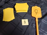 Yellow celluloid tray or stand with curved edges displayed on fabric surface alongside a number 5 paper tag.