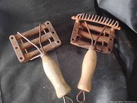 Two antique horse grooming brushes lying on a black fabric background, showing rust on metal parts and wooden handles with loops at the end.