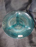 Photo of a round partitioned glass dish in blue-green carnival glass with three dividers and ribbed texture.