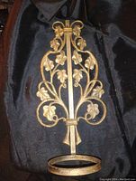 Front view of gold painted cast iron flower pot holder showing decorative vine and leaf motifs and circular base.