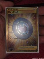 Close-up of the Dark Patch Trainer card, showing gold foil and holographic full art design.
