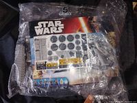 Sealed plastic bag with LEGO Star Wars Millennium Falcon instruction manual and decals visible inside.
