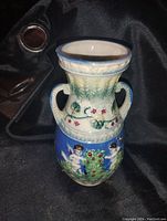 Full view of vase showing cherub and floral decoration with two handles and a blue and cream glaze.