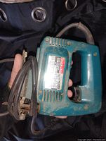 Side view of Makita electric jigsaw showing model label, power cord, and saw base plate with some rust and wear.