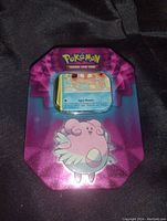 Purple Pokémon metal tin with Blissey character on lid, showing card through window.