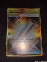 Close-up photo of Wishful Baton gold holo Pokémon Trainer item card showing detailed holographic patterns and text.