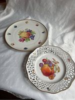 Two serving plates, one with pierced lattice rim and fruit motif, the other large round plate with fruit motif on white background