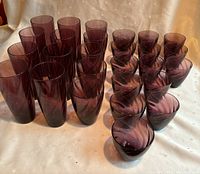 Front view showing all 24 glasses arranged in rows, showcasing various heights and sizes in dark amethyst purple glass with swirl pattern inside.