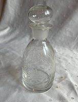 Full view of clear glass decanter with round stopper and etched cornflower design.