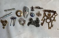 Full group shot of 12 assorted costume jewelry brooches on light fabric background, showing variety of designs and colors