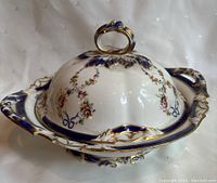 Full view of covered serving bowl showing lid handle, floral design, and ornate blue and gold accents