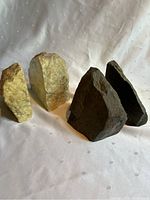 Two sets of stone bookends placed side by side on a white fabric surface. One set is light tan stone, the other dark gray stone. Both sets are roughly the same height and roughly triangular in shape.