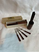 Full lot showing two cylindrical wooden holders each containing wooden cocktail picks, the original box, and four wooden-handled forks spread in front.