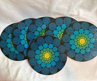 Six round midsize vintage metal trivets with colorful blue, green and yellow dot pattern on black background arranged in a fan shape