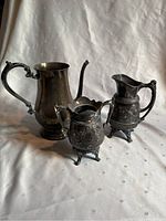 Three dark metal antique-style pitchers of differing sizes placed together on fabric background
