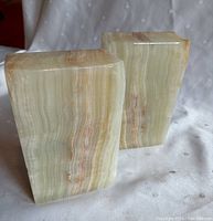 Front and side views of two onyx bookends placed on a white dotted fabric background showing natural banding and coloration.