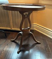 Oval wood side table from an angle showing lyre design pedestal and claw feet