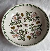 Top view showing full interior pattern of pink flowers, green leaves, yellow butterflies, and a bee in the center with a green leaf border around the rim.