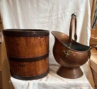 Wood barrel and copper pitcher on a white fabric backdrop, showing both items side by side for size and detail comparison.