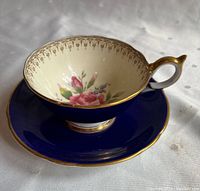 Side view of teacup showing floral design inside, blue exterior and gold trim on handle and rim.