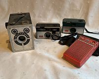 Overview image showing three vintage cameras and one red transistor radio on a cream-colored surface.