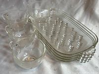 Overall view of the 4 clear glass mugs with handles and 4 rectangular clear glass plates with raised dot pattern and textured handles.