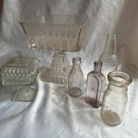 Full view of two vintage glass pedestal bowls and four vintage glass bottles on fabric background