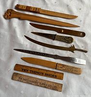 Full view of 8 letter openers arranged with 2 wooden rulers showing clear branding and dated appearance