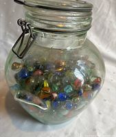 Clear glass jar of about 8x10 inches filled with assorted colorful vintage marbles, showing the variety and condition of the marbles inside.