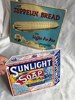 Close-up photo with hand holding the Sunlight Soap metal sign, showing its 3D soap box shape and vintage graphics.