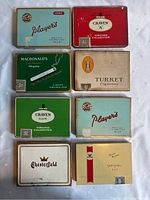 All 8 vintage cigarette metal tins arranged on a flat surface, showing branding and condition.