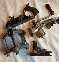 Photo showing wood hand plane, manual meat grinder, small metal clamp, and other vintage tools.