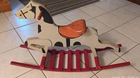 Photo showing side angle of the wooden rocking horse, highlighting the black and white design, orange saddle, and red rocker base