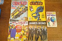 Four assorted magazines including two Cracked magazines, Simpsons 30 Years edition, James Bond special edition, and one Mad magazine book 'Mad's Sick World'. Visible wear on edges and corners.